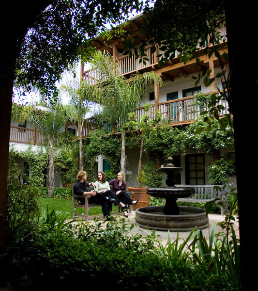 Outside view of three women sitting on the bench in front of the water fountain, talking