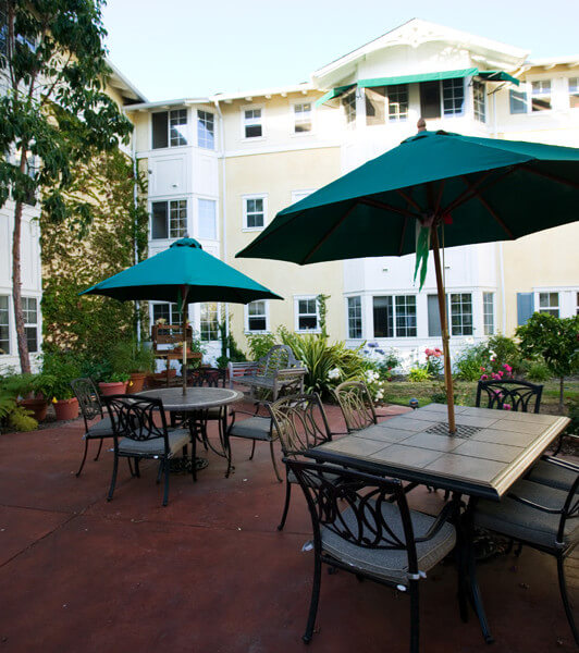 Outside shot of chairs and tables with umbrellas, with the units in the background