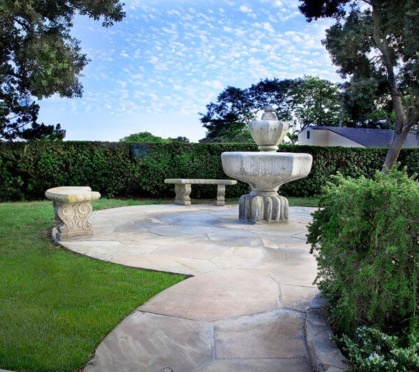 Outside view of a stone fountain and benches surrounded by a hedge
