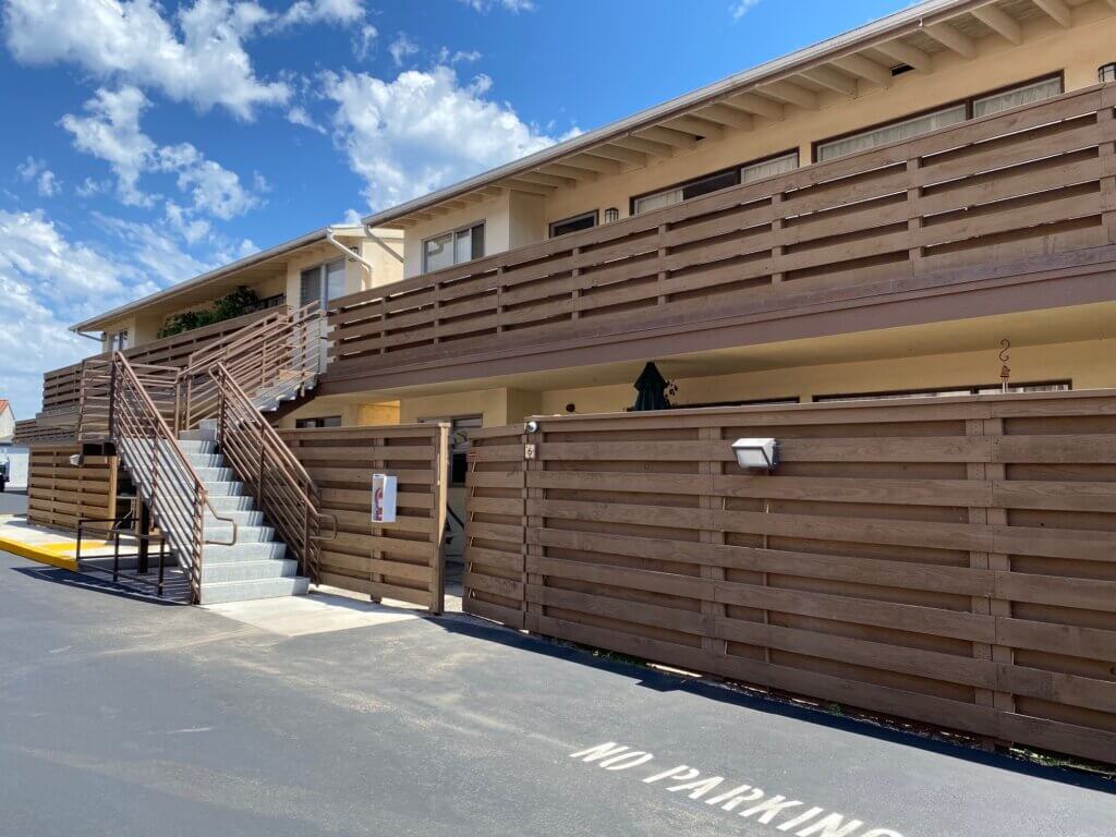 Front of building, with staircase leading to second floor, wood fencing.